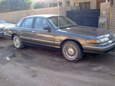 1992 Ford Crown Victoria - Three-quarter front passenger-side view of a dark gray aero-body Ford Crown Victoria sedan with a white roof, chrome lace-style alloy wheel…