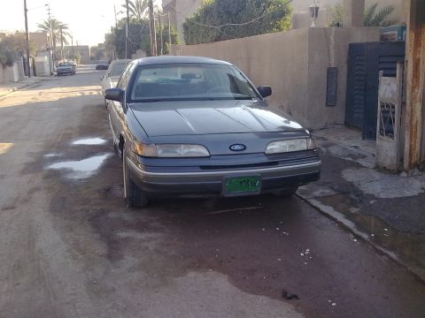 1992 Ford Crown Victoria - Front view of a gray aero-body Ford sedan with the Ford blue oval on the grille, composite headlights and a green license plate with Arabic…