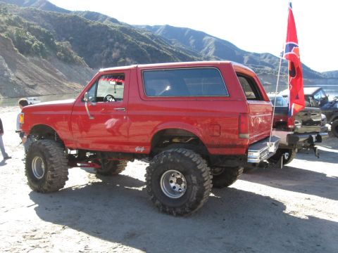 1987 Ford Bronco - This lifted 1987 Ford Bronco features aggressive off-road tires and a prominent stance, seen here with other vehicles in the background.
