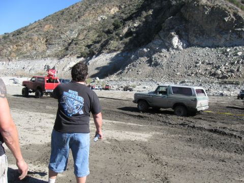 1987 Ford Bronco - Off-road vehicles navigate a muddy terrain, with a gray Ford Bronco and a red truck visible.