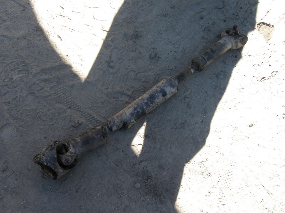 Dirty removed driveshaft with U-joints lying on dusty ground