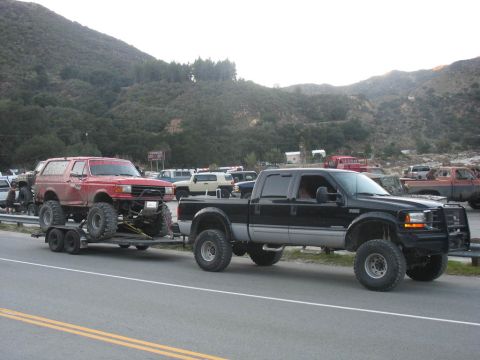 1987 Ford Bronco - A lifted 1987 Ford Bronco is transported on a trailer by a black Ford F-250 truck on a roadside.