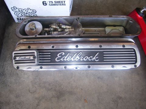 1990 Ford Mustang - Edelbrock valve cover and a set of spark plugs are displayed on a concrete surface.