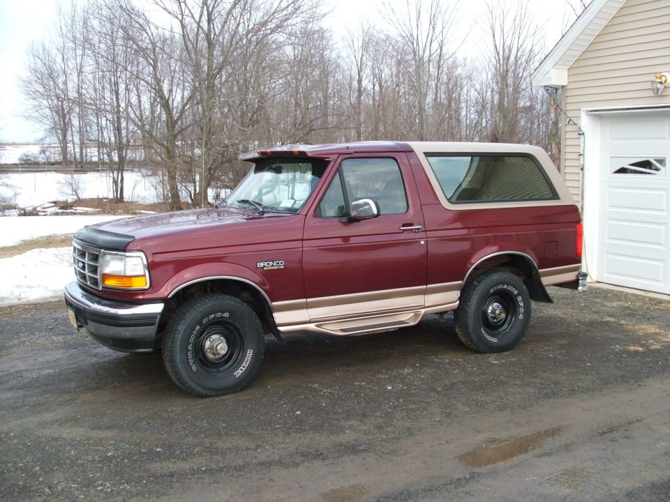 Maroon and tan two-tone Ford Bronco SUV parked on gravel driveway by a white garage in winter
