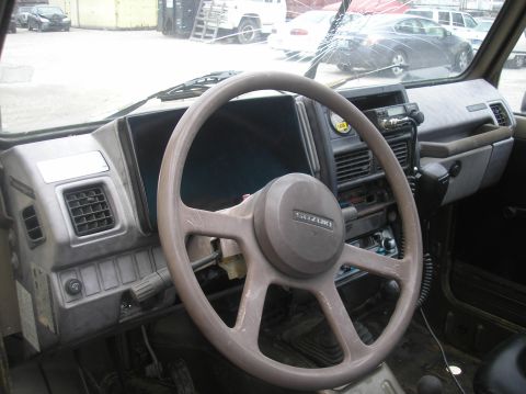 1987 Suzuki Samurai - The interior of a Suzuki Samurai shows its dashboard, steering wheel, and a CB radio, with other vehicles visible through the cracked winds…