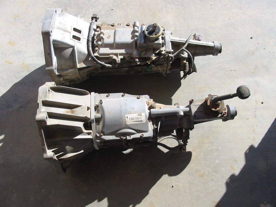 Two transmissions, one with a Tremec label, on a concrete surface