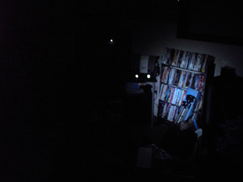 Dark room interior with a bookshelf filled with items and two glowing white lights resembling eyes