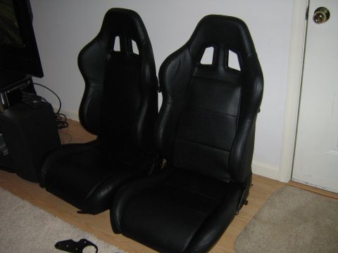 1990 Ford Bronco - A pair of black racing seats are shown indoors, with a door and a rug in the background.