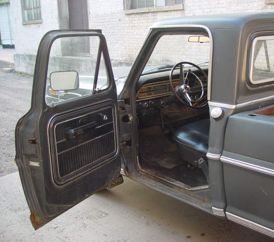 1969 Ford pickup truck interior with open driver's door, showing dashboard, steering wheel, and seat. "FORD" text visible on door sill