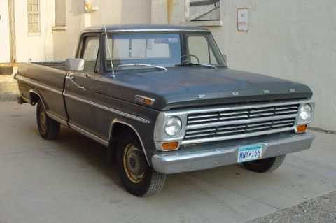 1969 Ford Fairlane - This dark-colored Ford pickup truck is parked outside a building. The grille and headlights are prominent features.