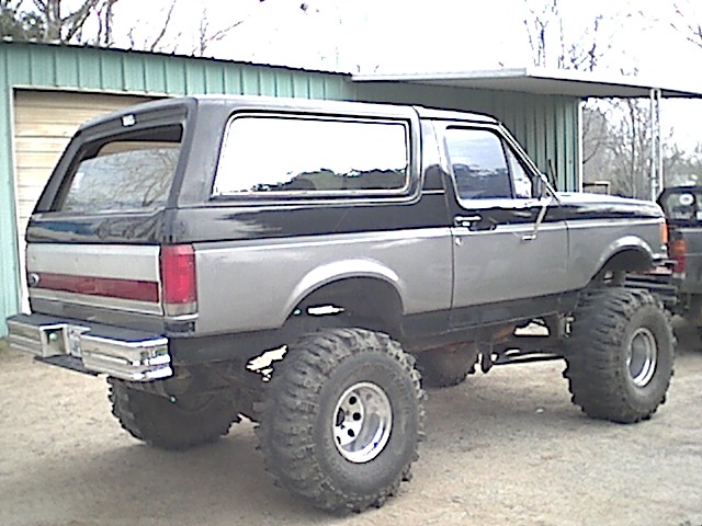 Lifted 1987 Ford Bronco with large off-road tires, two-tone paint, and chrome bumper