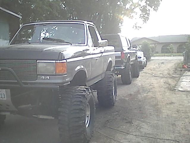 Lifted pickup trucks lined up, front one has a brush guard and big tires