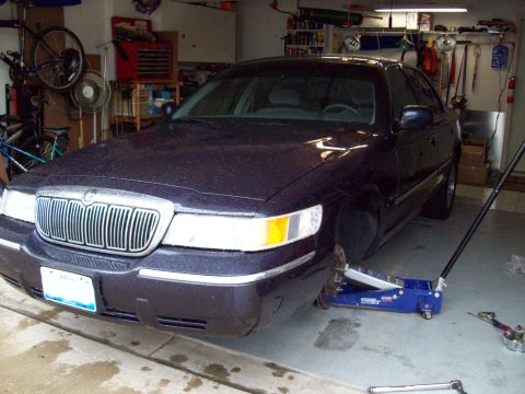 1999 Mercury Grand Marquis - Garage scene with a 1999 Mercury Grand Marquis being serviced, front wheel removed.
