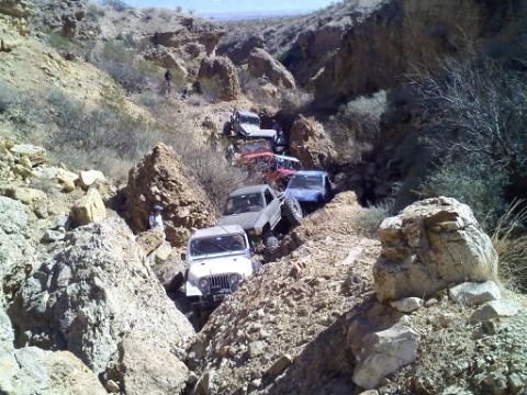 1993 Ford Bronco - Multiple off-road vehicles are seen traversing a challenging, rocky terrain in a desert canyon.
