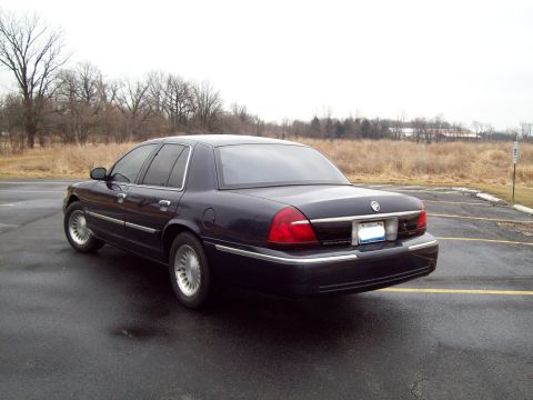 1999 Mercury Grand Marquis - This dark blue sedan, likely a 2003 model, is seen from the rear in a parking lot.