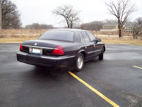 1999 Mercury Grand Marquis - A dark sedan is parked on an asphalt lot with yellow lines on the ground.