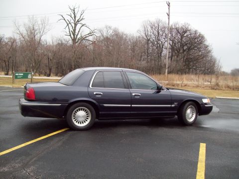 1999 Mercury Grand Marquis - A dark blue 1999 Mercury Grand Marquis is shown from the side in an overcast outdoor setting.