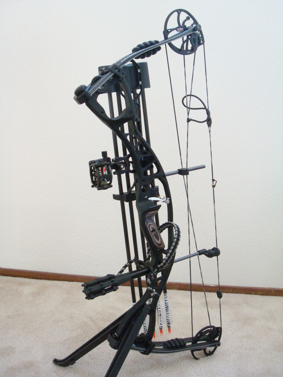 Black compound bow with quiver and arrows attached, shown from a 3/4 front angle