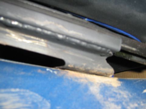 1990 Ford Bronco - A close-up view of a rusted metal frame, possibly from a vehicle's undercarriage, with visible blue paint and wiring.