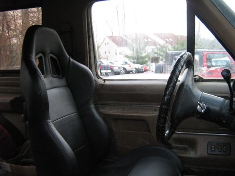 1990 Ford Bronco - The interior of a 1990 Ford Bronco features racing seats and a steering wheel, with other vehicles visible through the window.