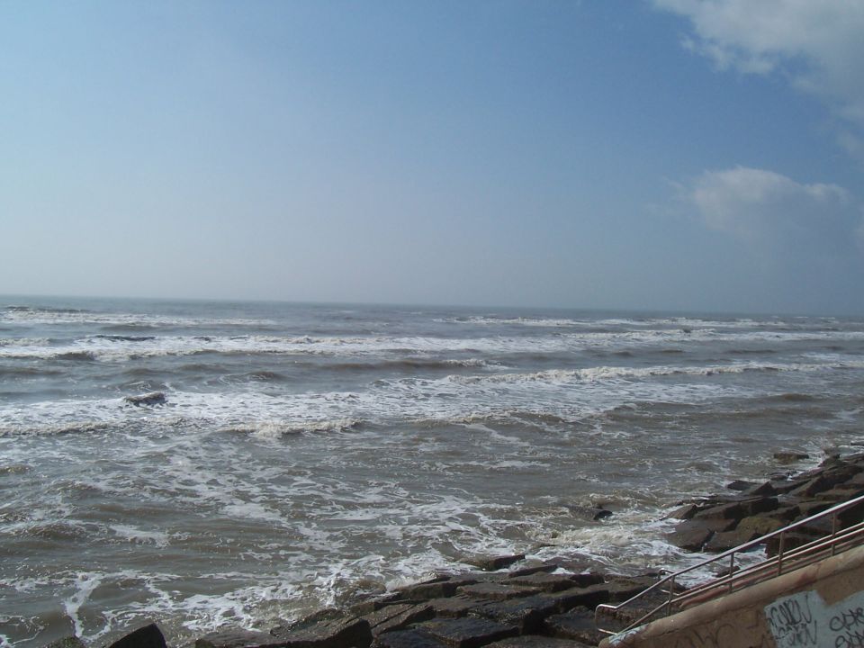 Ocean waves roll onto a shore lined with large rocks and a concrete embankment with graffiti