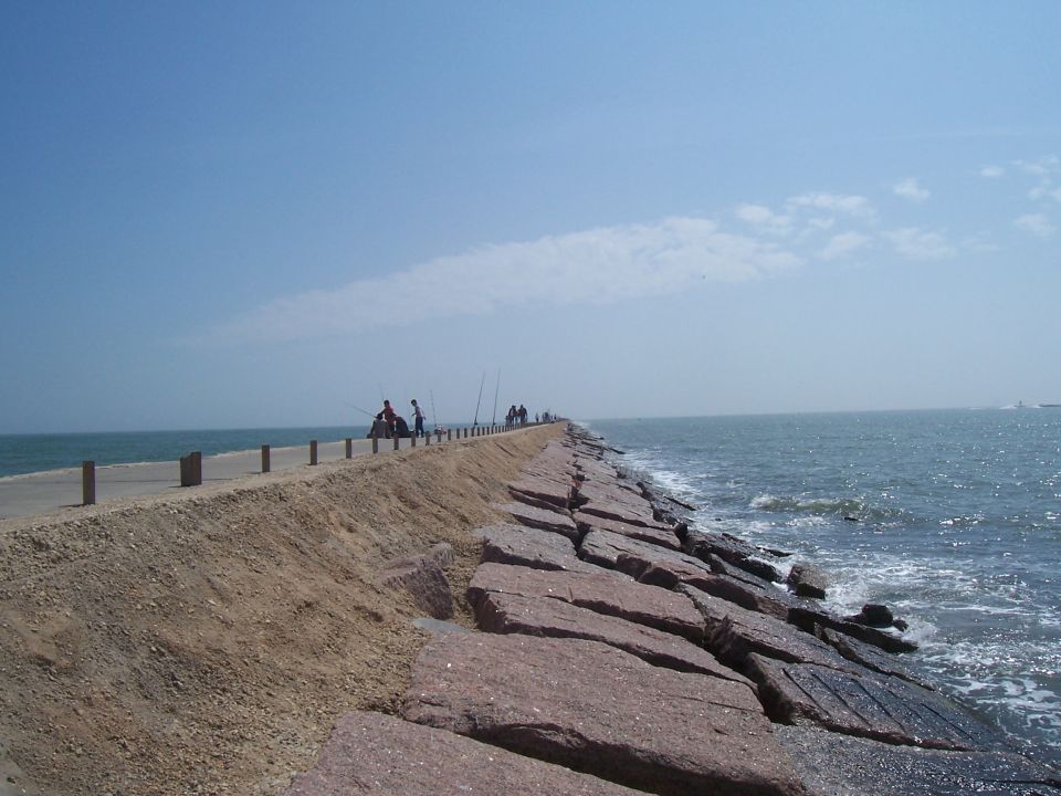 Long pier with large rocks on the right and a sandy embankment on the left, with several people fishing