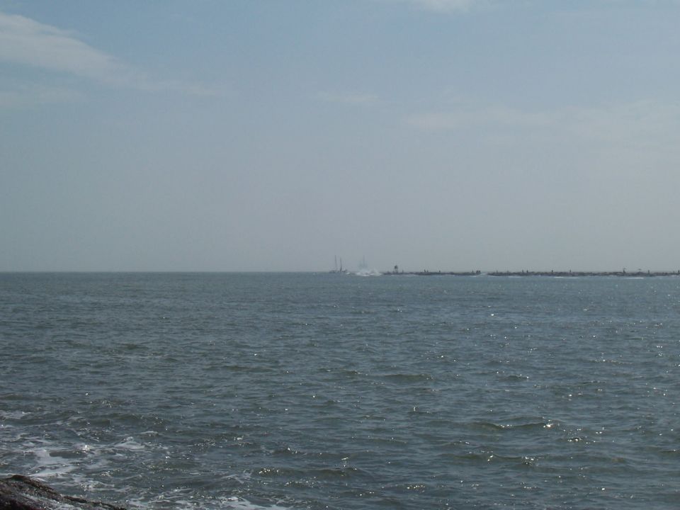 Distant boats on the water near a breakwater under a hazy sky