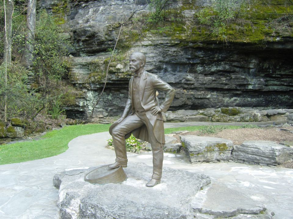 Bronze statue of a man in a suit standing on a rock in front of a cliff