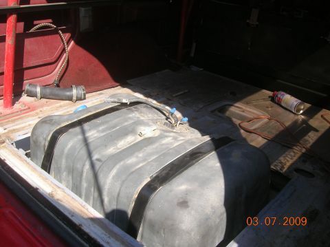 1985 Ford Bronco - The interior of a vehicle shows a large fuel tank, with a hose and a can of spray paint nearby.