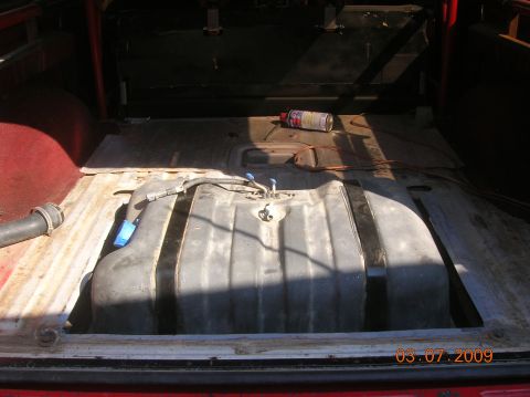 1985 Ford Bronco - The interior of a vehicle shows a large fuel tank in the cargo area, with some tools and a can of spray paint nearby.