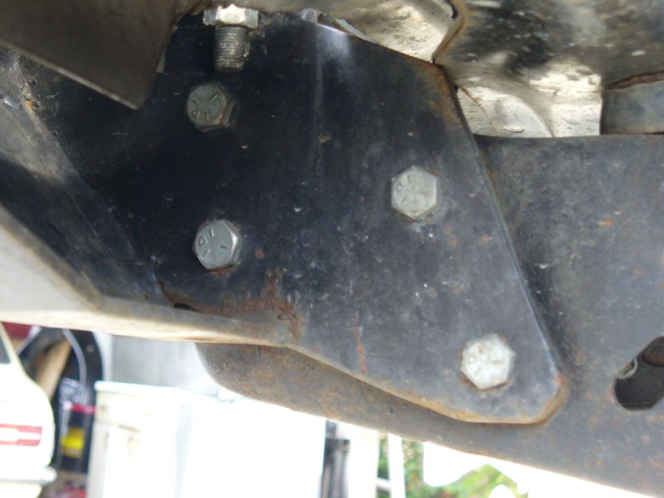 Close-up of a black metal bracket with several hex bolts, showing rust and wear