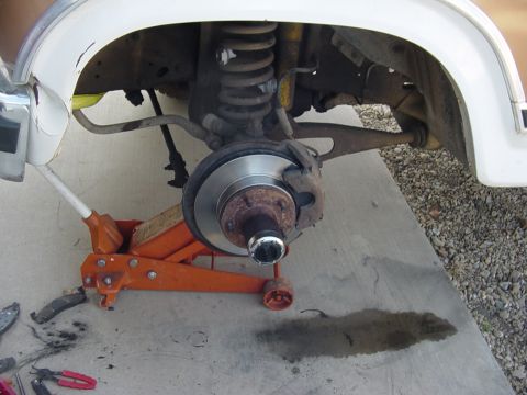 1982 Ford Bronco - The front suspension and brake assembly of a vehicle are shown, with a floor jack underneath.