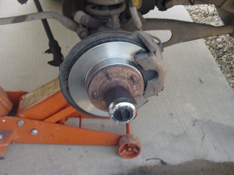1982 Ford Bronco - Close-up of a vehicle's front wheel hub and brake assembly, supported by an orange hydraulic jack.