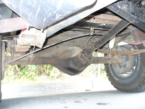 1978 Ford Bronco - Underside view of a vehicle's rear axle, driveshaft, and suspension system, showing leaf springs and shock absorber.