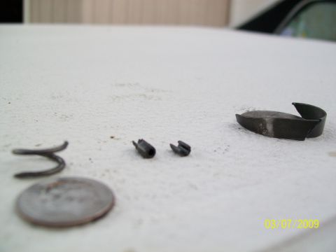 1972 Ford Ranchero - Several small metal automotive parts and a coin are laid out on a white surface.