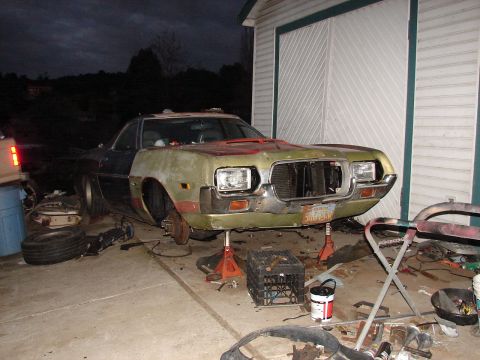 1973 Ford Ranchero - A green Ford project car photographed at night on jack stands outside a garage, its front end disassembled with headlights and grille partl…