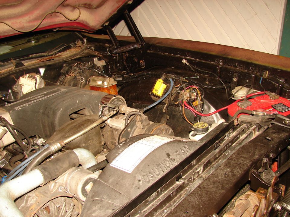 Open engine bay with CAUTION FAN shroud, red battery, alternator and wiring on core support