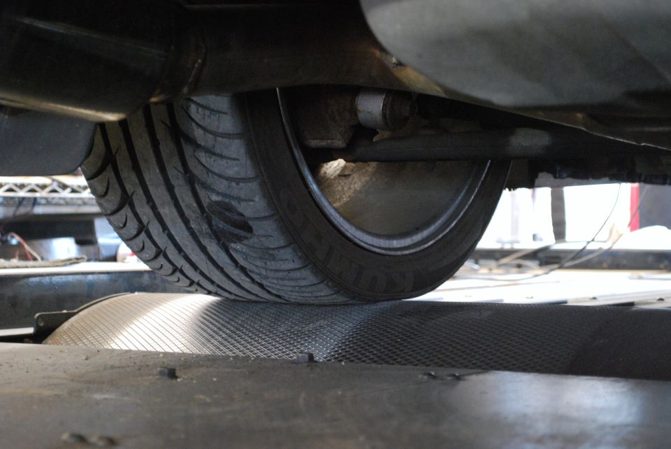 Close-up of a car tire on a dynamometer roller, showing underbody components