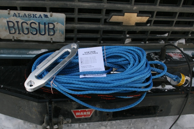 Blue winch line and silver shackle on a vehicle bumper with an Alaska license plate.