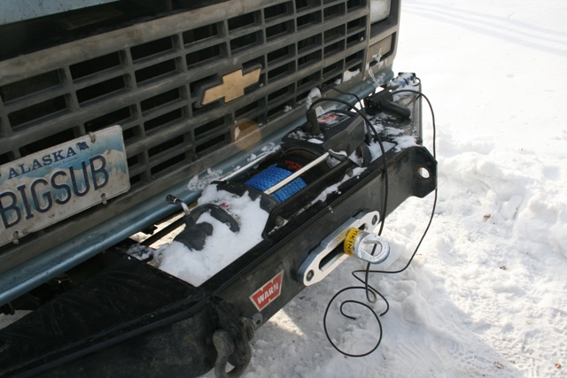 Chevrolet truck front bumper with winch and Alaska license plate "BIGSUB" in snow.