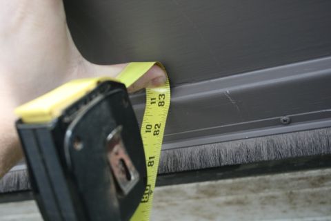 1990 Chevrolet Suburban - A yellow measuring tape is held against a dark gray metal surface, possibly a vehicle door or panel, with a brush seal visible below. The t…