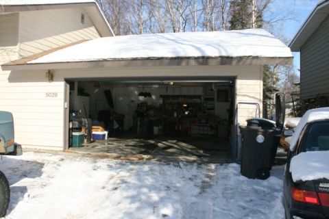 1990 Chevrolet Suburban - two-car detached garage with snow on the roof, open door revealing a workshop, address 5029, with cars and trash bins outside.