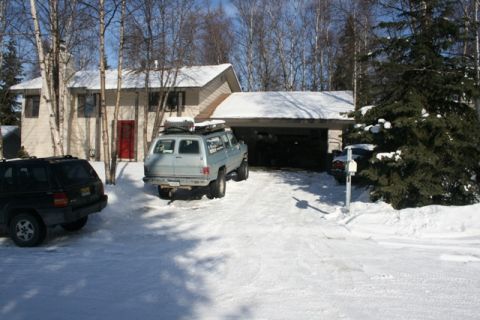 1990 Chevrolet Suburban - A light blue Chevrolet Suburban with a roof rack is parked in a snow-covered driveway in front of a house. A black SUV is parked to the lef…