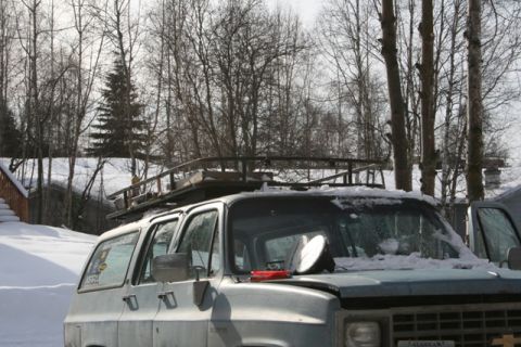 1990 Chevrolet Suburban - A light blue Chevrolet Suburban is parked in a snowy setting with a roof rack loaded with items. The front of the vehicle shows a circular…
