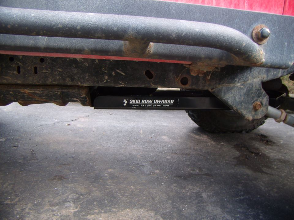 Black skid plate with "SKID ROW OFFROAD" text mounted under a red Jeep Wrangler frame.