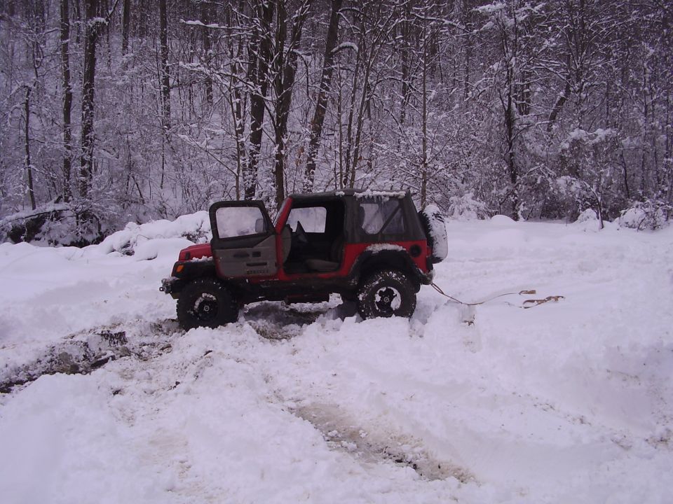 Red and gray Jeep Wrangler stuck in snow with doors open and tow strap attached.
