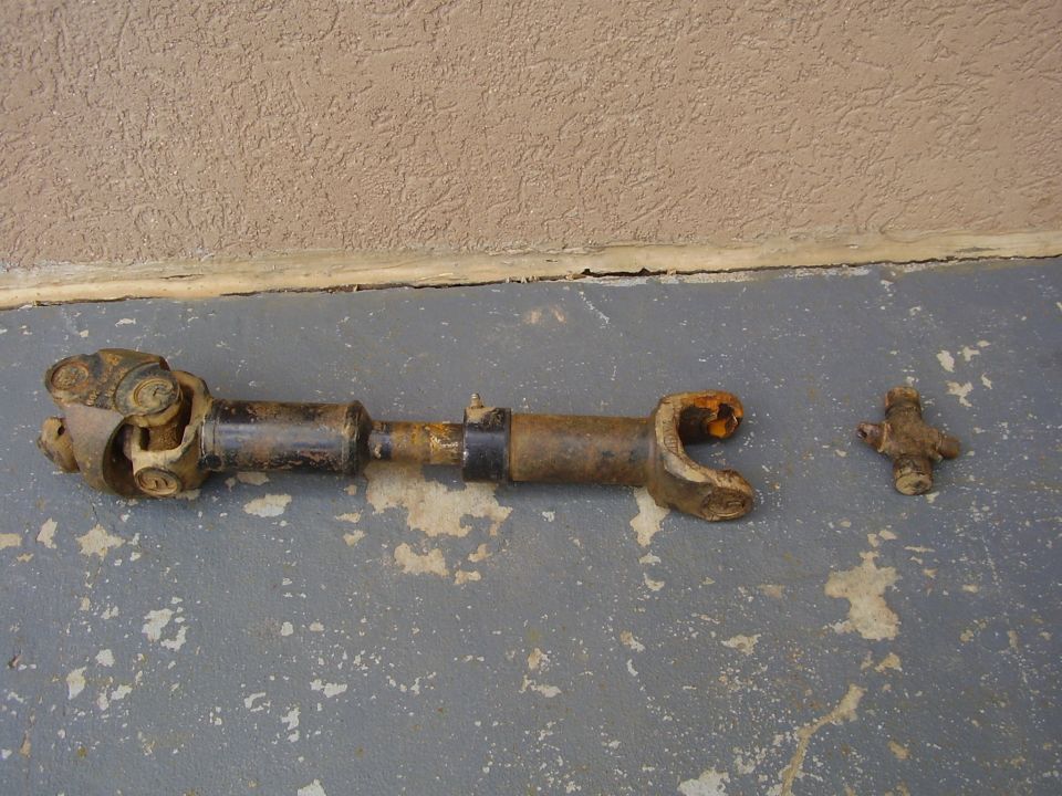 Rusty driveshaft with universal joint and separate universal joint cross on concrete.