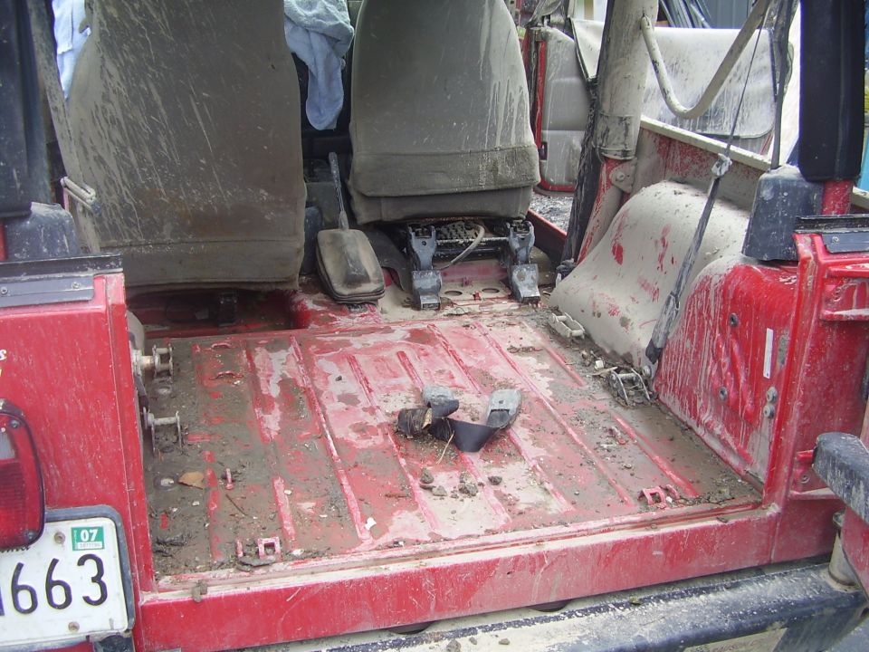 Mud-covered interior of a red Jeep Wrangler, showing the floor and seats.