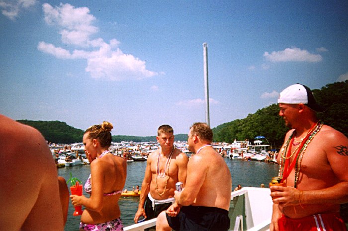 People in swimwear on a boat deck at a crowded lake party cove