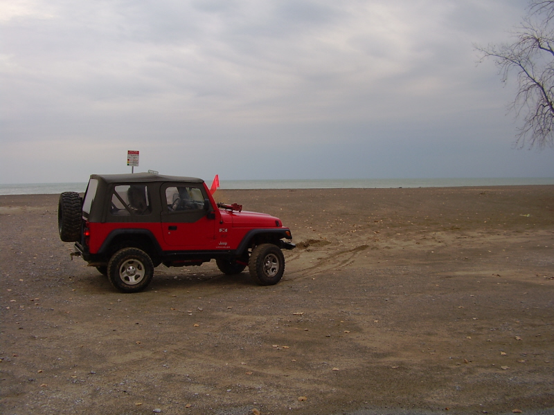 Red Jeep Wrangler parked on a beach near the water.
